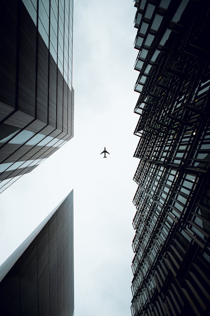 Home A dramatic view of an airplane flying above modern skyscrapers in London, UK.